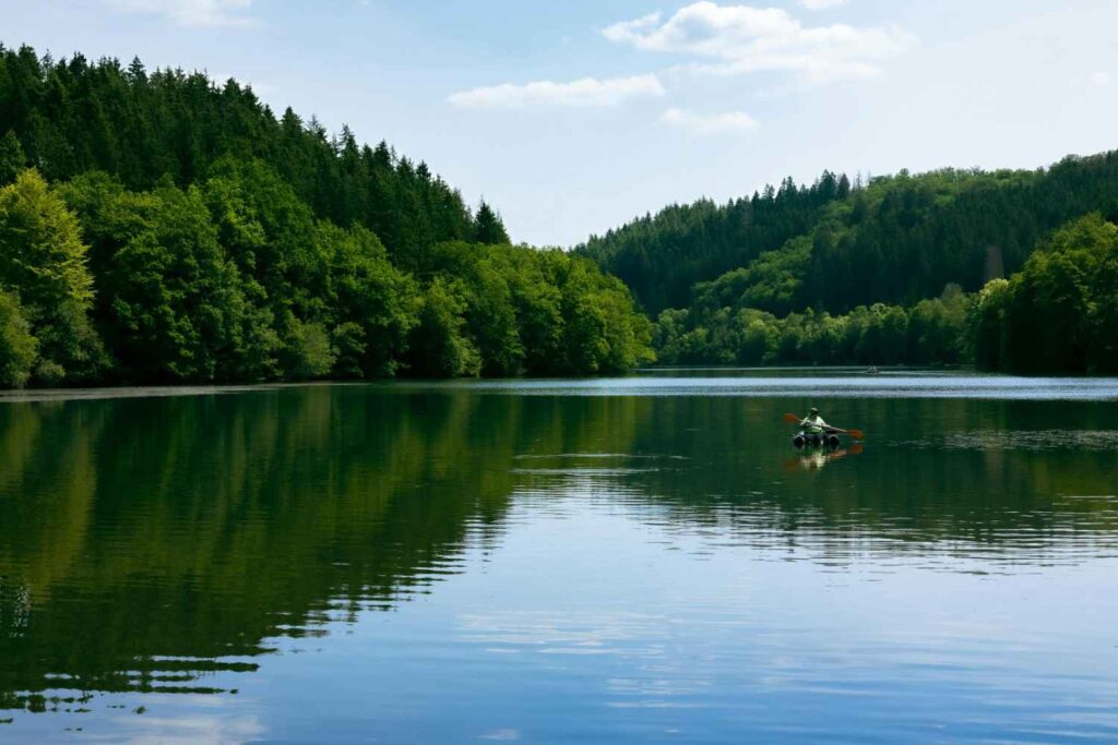 solo kayaker paddling inflatable kayak on calm lake with forest background