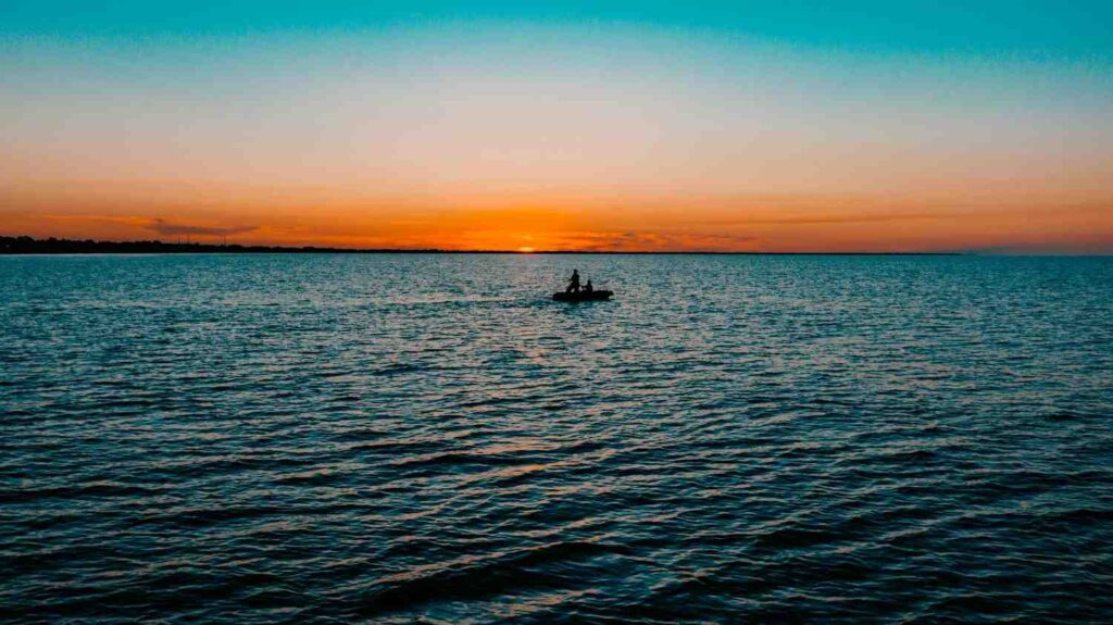 Silhouette of two people on kayak fishing on open water during golden sunset