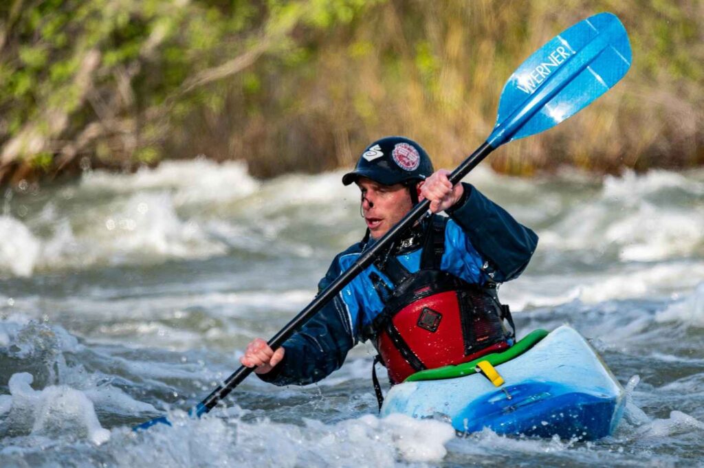 Kayaker using high-angle paddle stroke in fast whitewater rapids