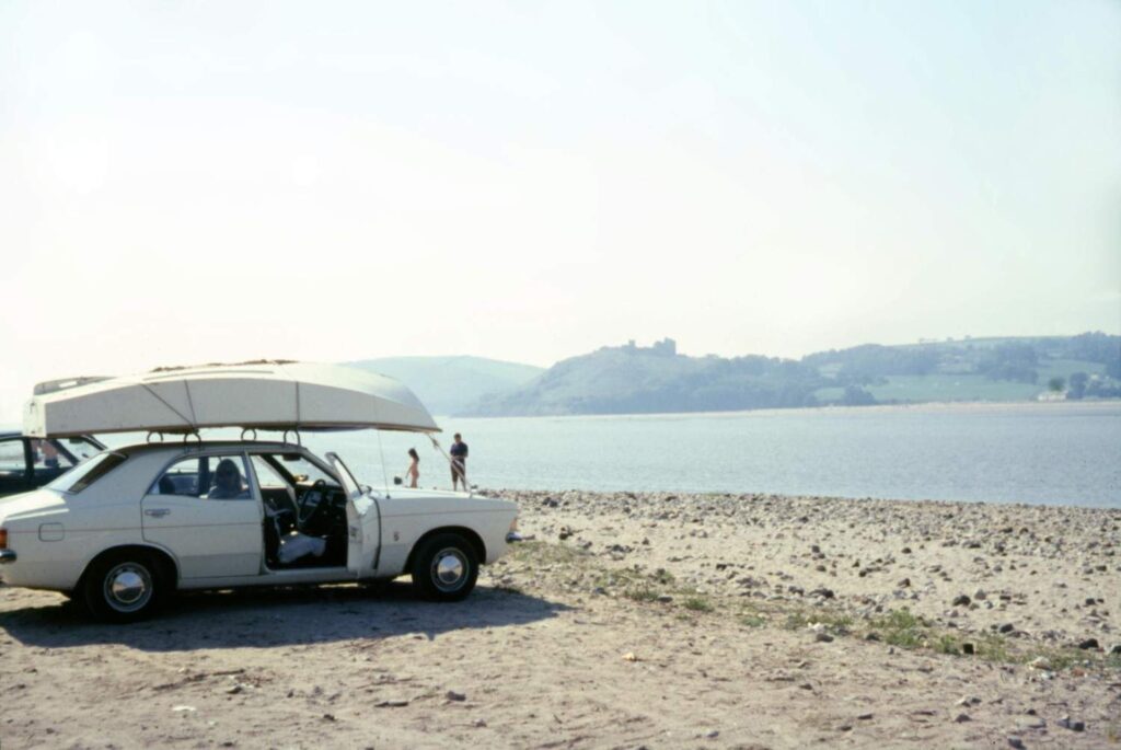 White car with kayak strapped on roof rack parked near beach