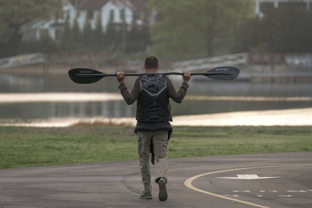 Man carrying Werner carbon fiber kayak paddle on shoulders near lake