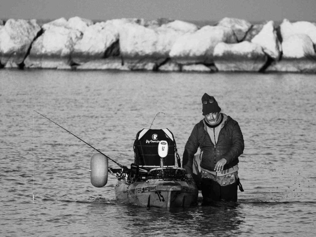Angler standing next to heavy loaded fishing kayak with rods and gear in saltwater