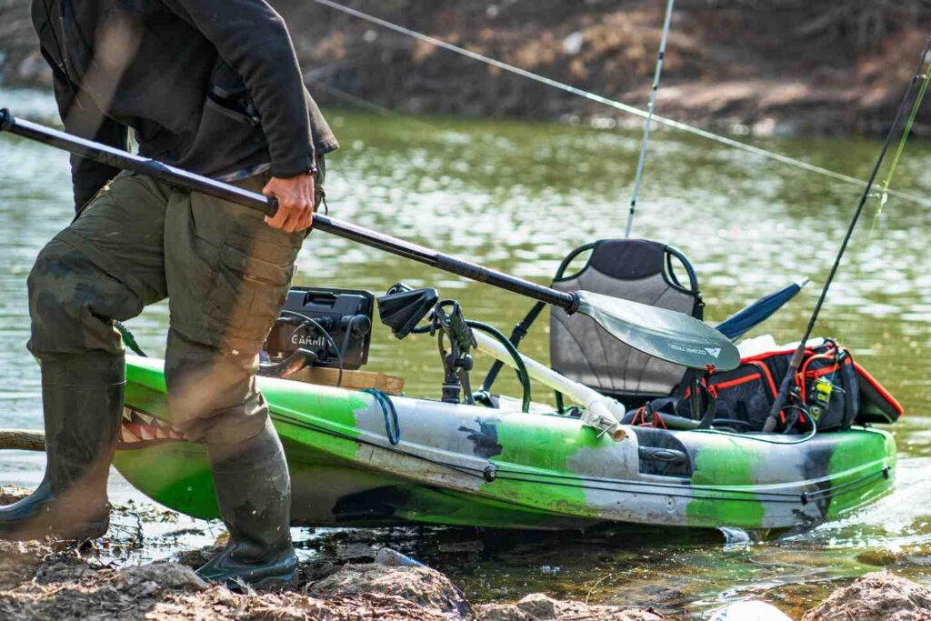 Green fishing kayak with Garmin fish finder and fishing rods at riverbank