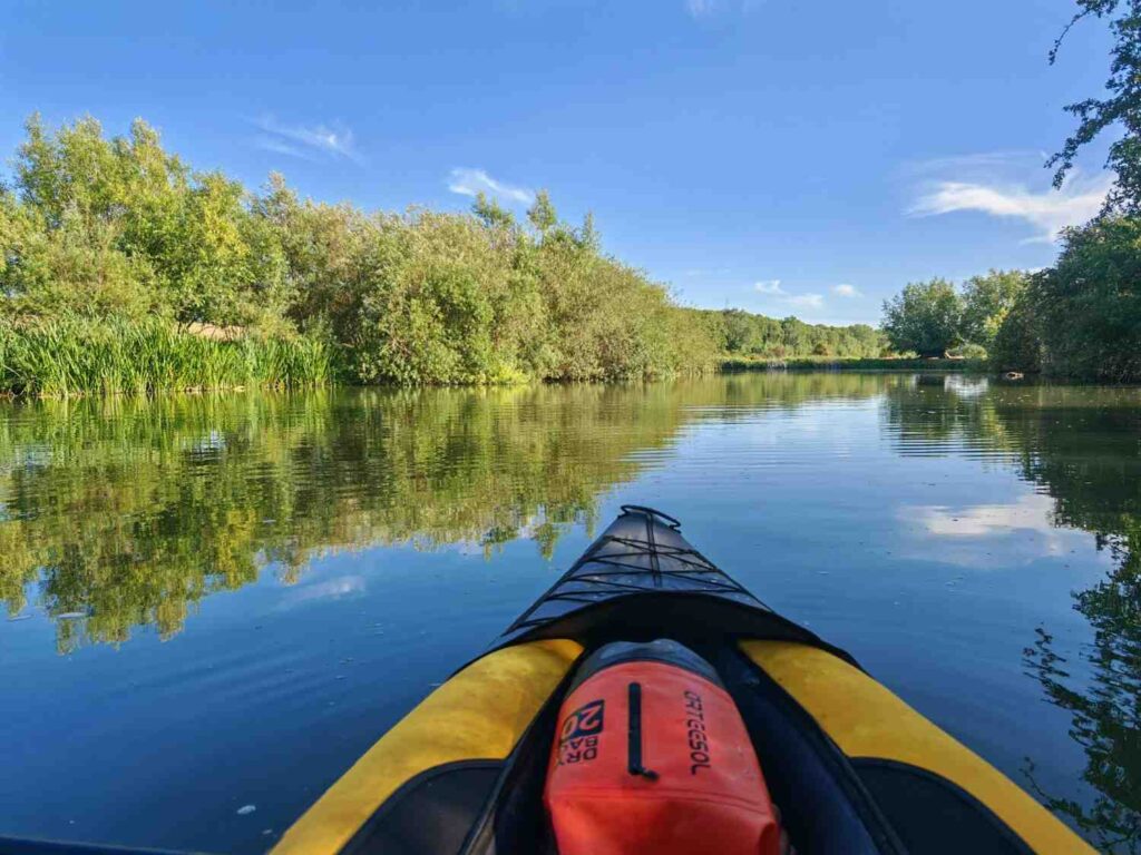 First-person view of a yellow inflatable kayak on a calm green river