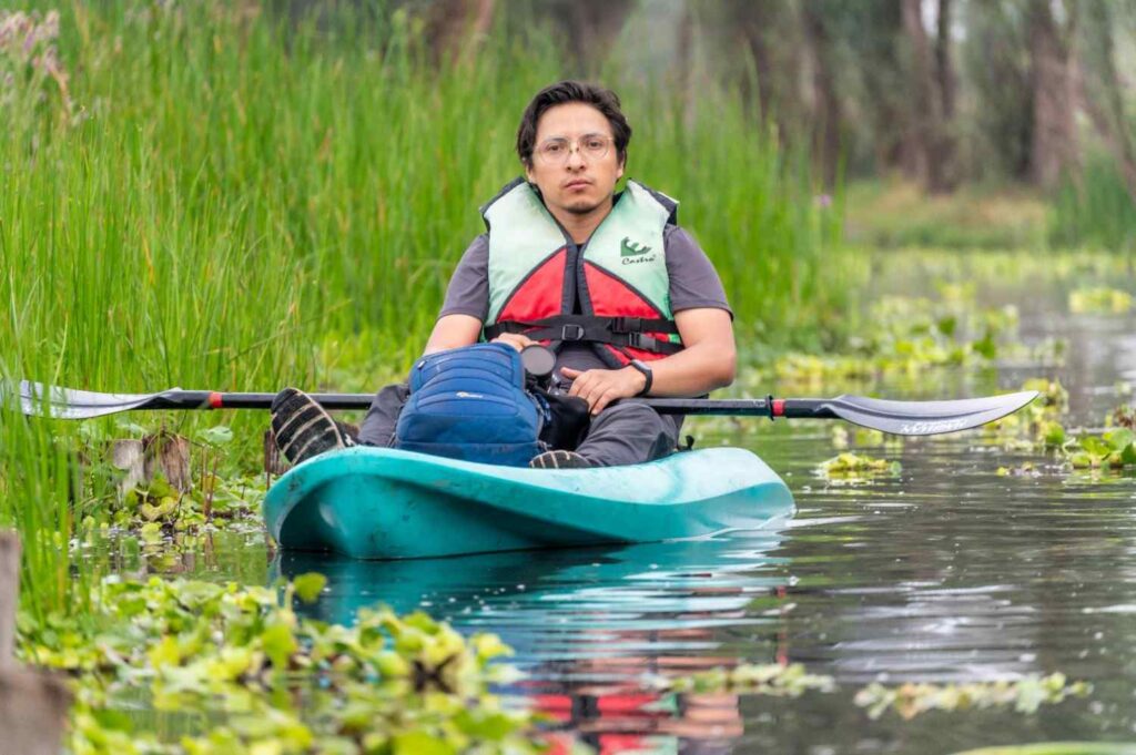 Man sitting in teal kayak with backpack paddling through marsh wetland