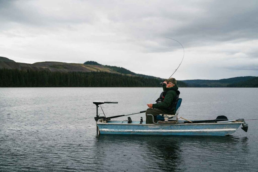 Angler fishing from small boat with fish finder and trolling motor mounted on lake