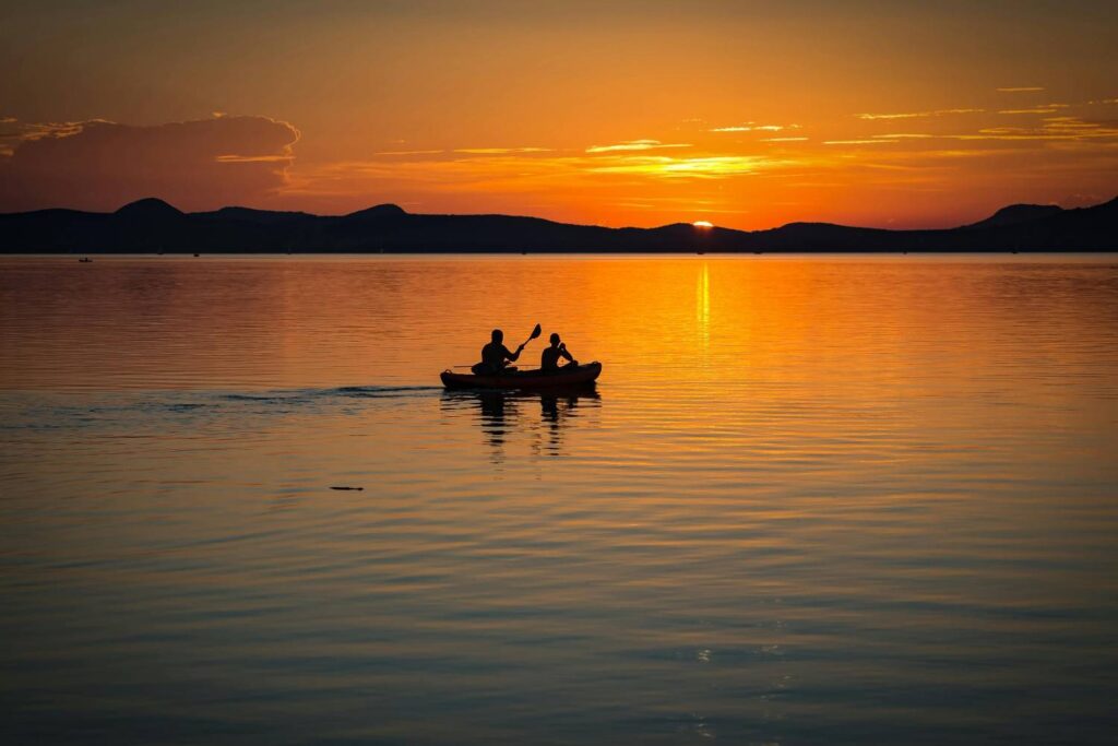 Silhouette of two kayakers paddling on calm lake during golden sunset