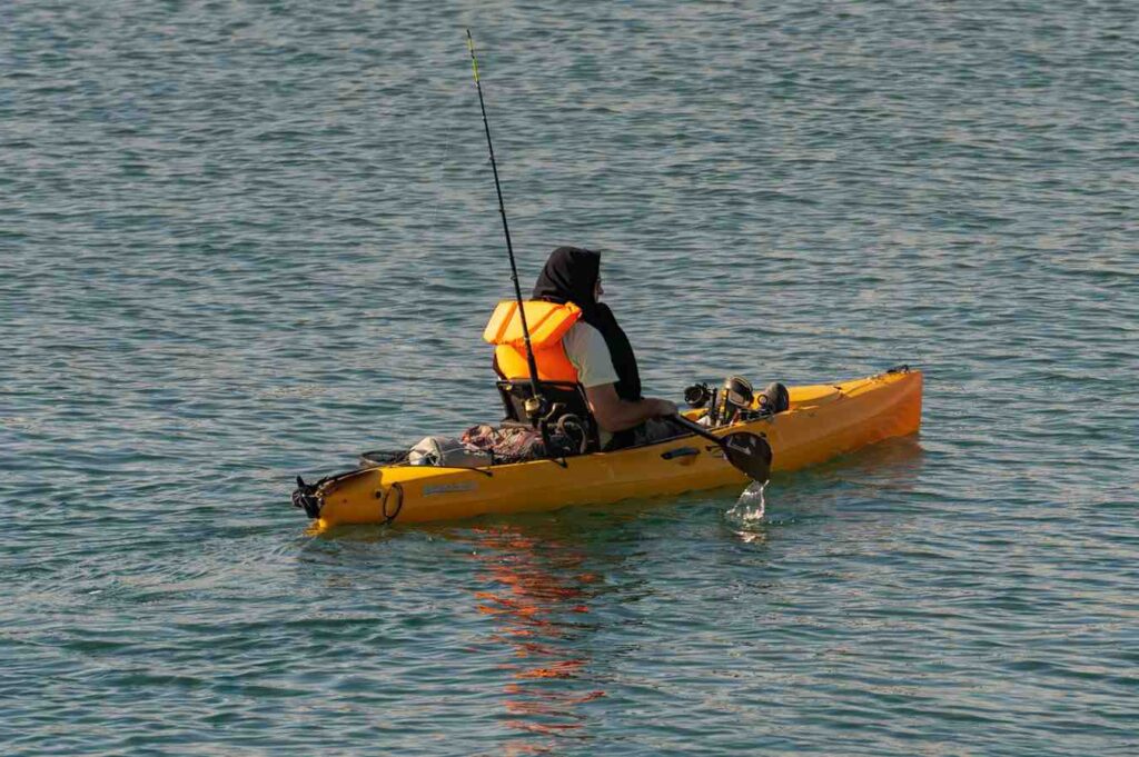 Angler fishing from yellow pedal drive kayak on open water with fishing rod