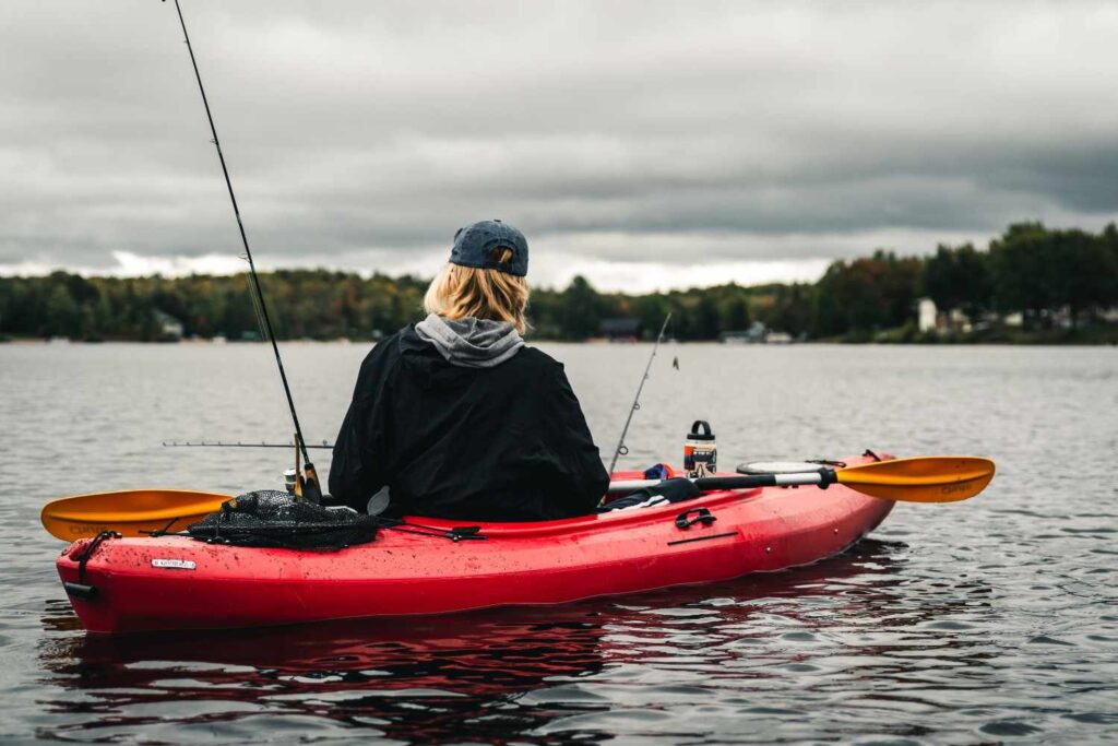 Back view of angler in red fishing kayak with multiple rods set up waiting on a calm overcast lake