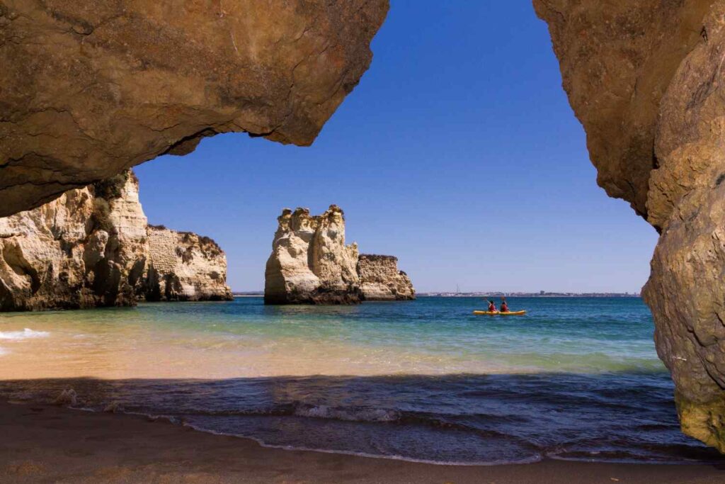 Two people paddling a yellow sit-on-top kayak through calm turquoise ocean water framed by dramatic limestone rock formations