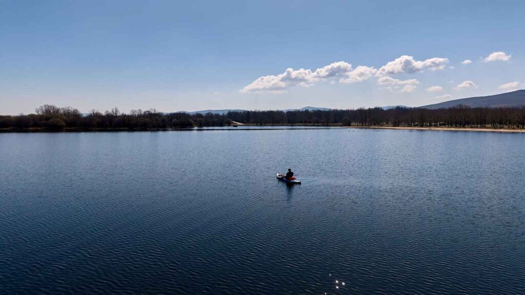 Aerial view of solo angler in a kayak positioned perfectly in the center of a wide calm blue lake under clear sky