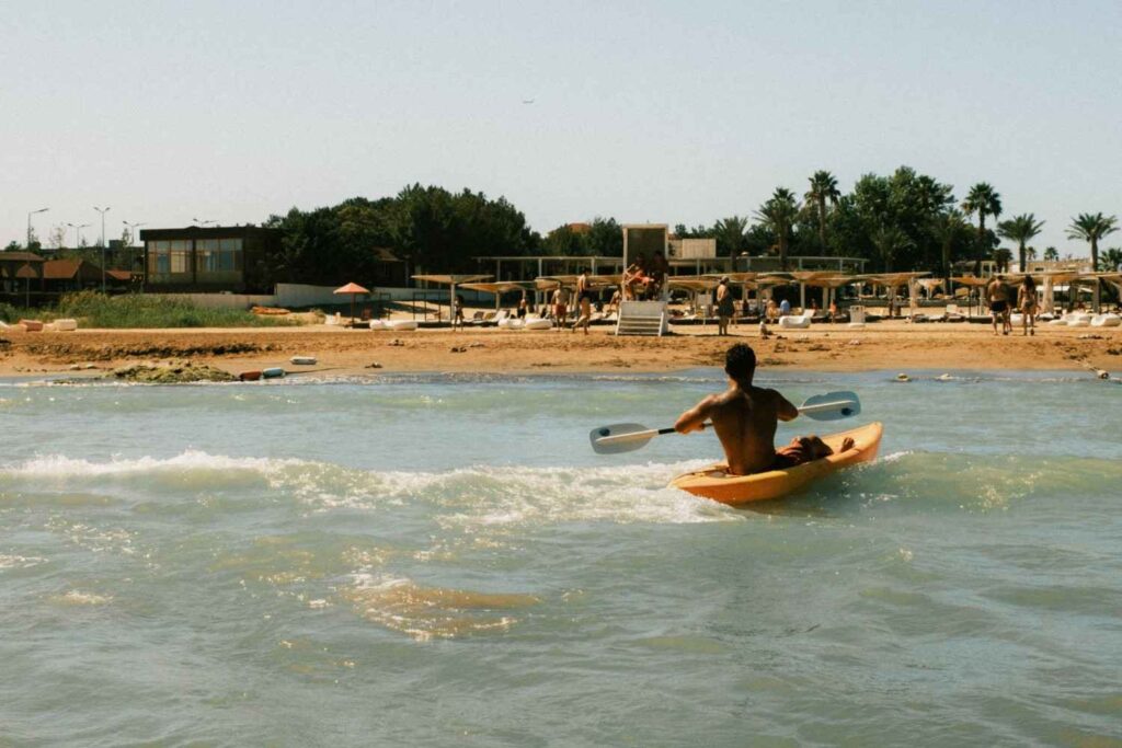 A man paddling a yellow kayak through breaking shore waves at a busy beach resort on a sunny day