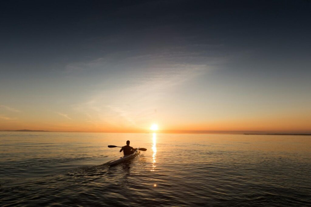 A lone kayaker silhouetted against a beautiful golden sunset paddling across calm open water