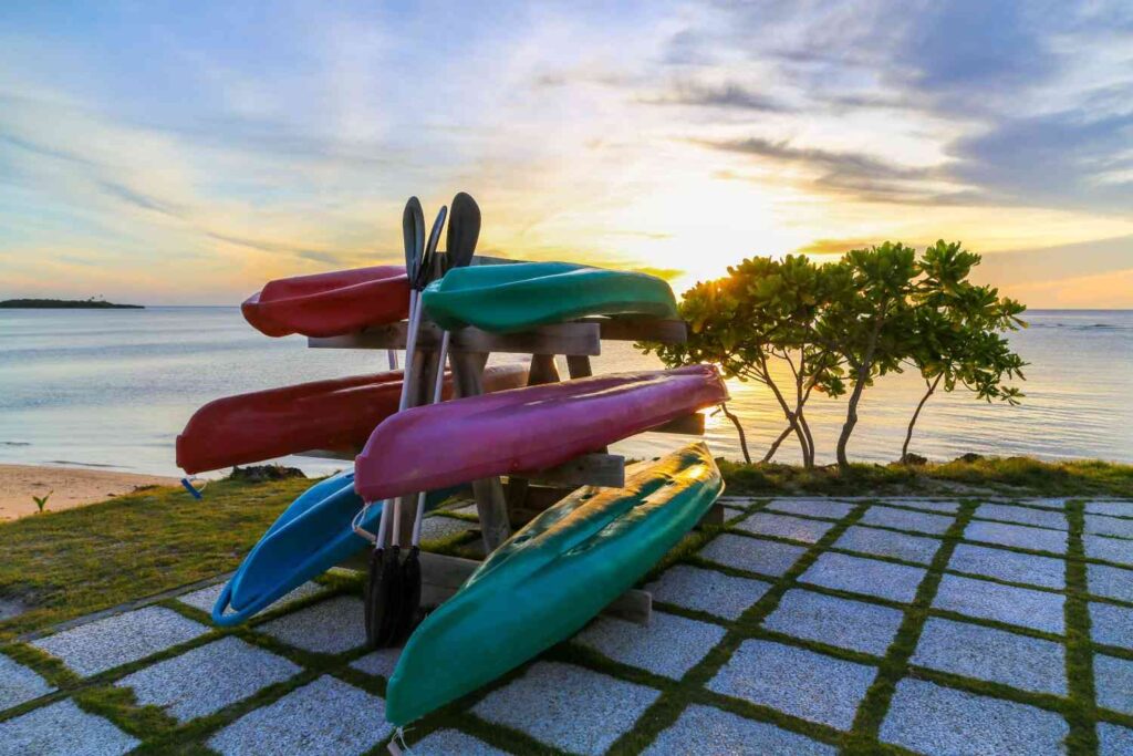  Multiple colorful kayaks stored on a wooden rack near a beach at golden sunset, ready for next paddle
