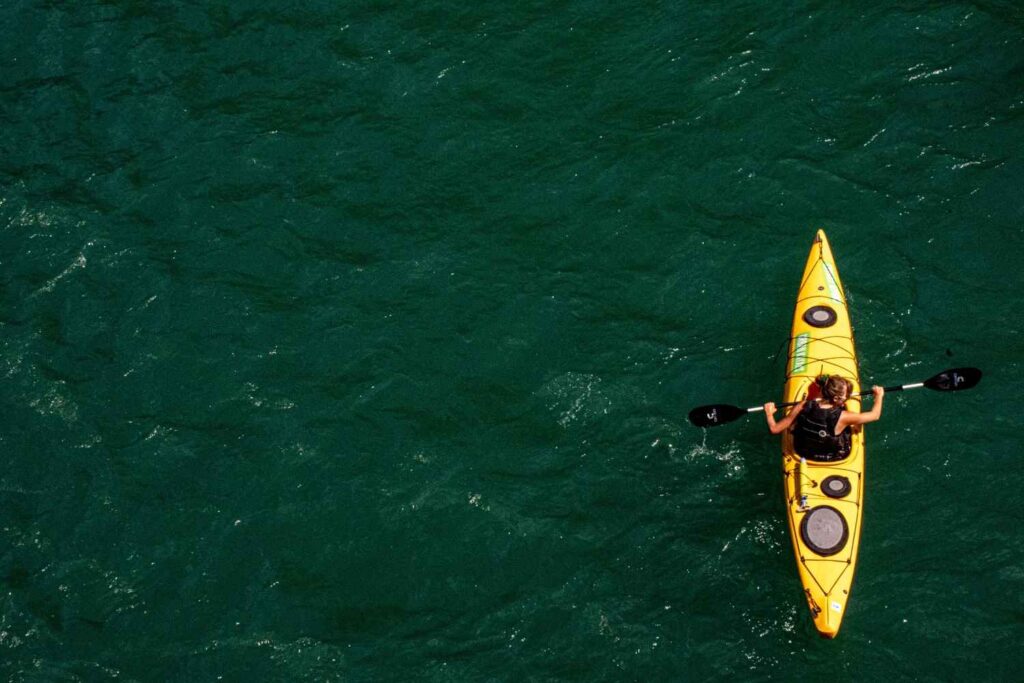 Aerial view of a woman paddling a yellow sea kayak alone on deep green water