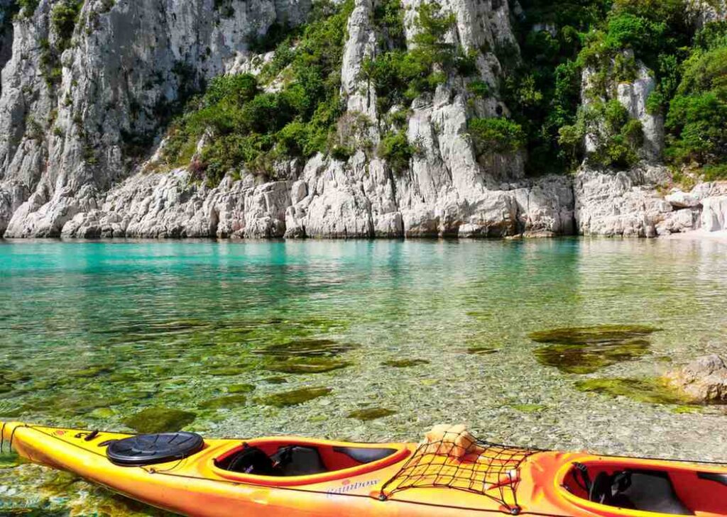 Two colorful sea kayaks resting on smooth rocks beside crystal clear turquoise water with dramatic rocky cliffs in the background