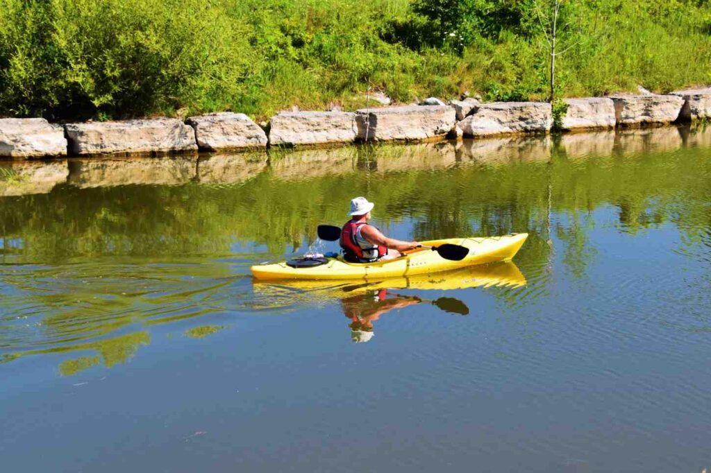 An older solo kayaker in a yellow kayak paddling peacefully on calm water on a sunny day