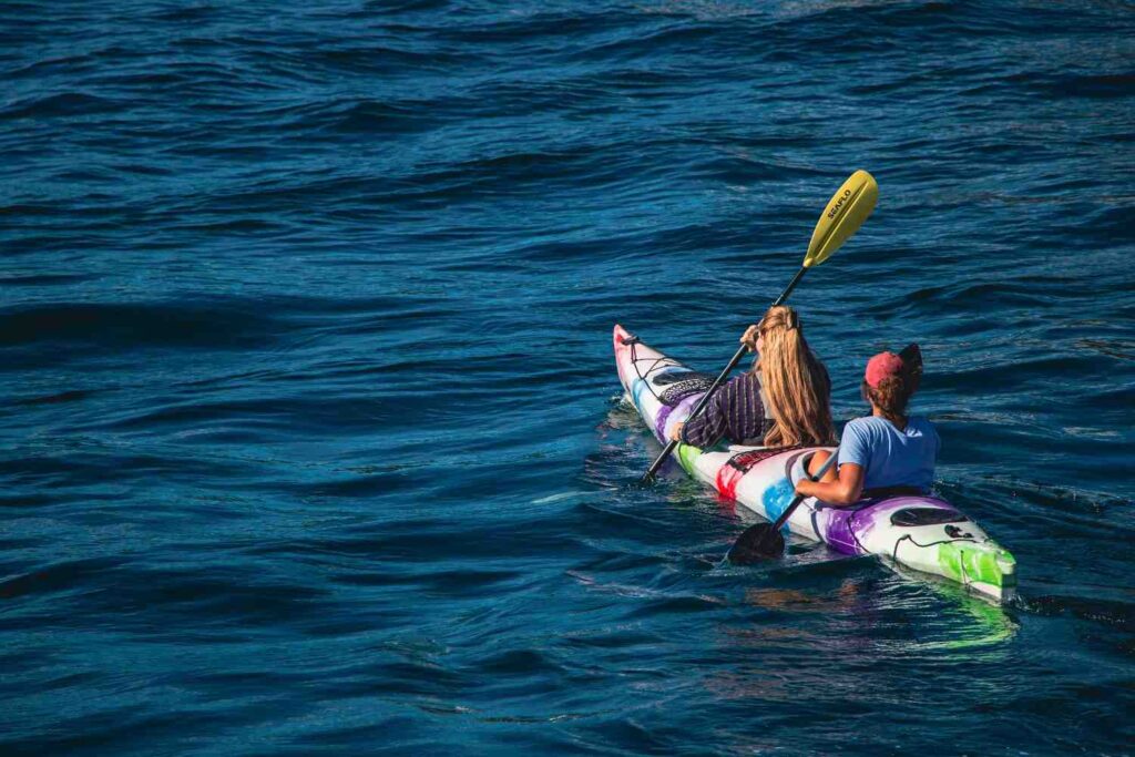Two people paddling a colorful tandem kayak on open blue water