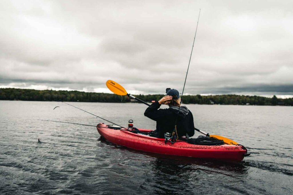 Angler in red fishing kayak shielding eyes under cloudy summer sky with rods deployed