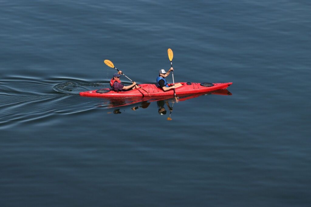 Two men paddling a red tandem kayak across a calm lake