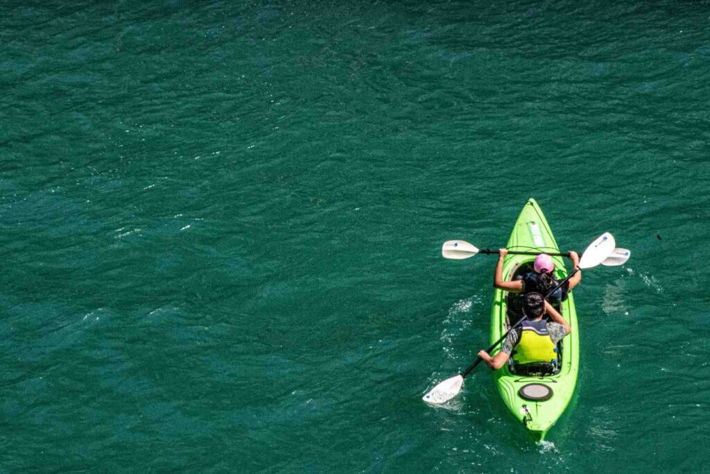 Aerial view of two people in life jackets paddling a green tandem kayak together on clear teal water