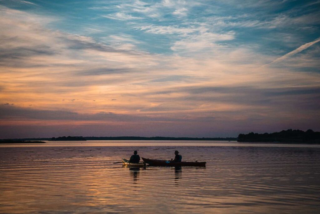 Silhouette of two kayakers paddling on calm water under a dramatic golden sunset sky