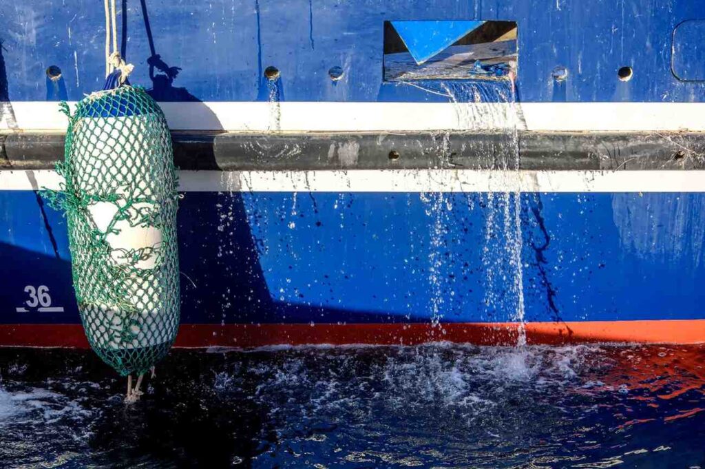 Close-up of water draining out through a boat hull opening, illustrating how a bilge pump discharges water