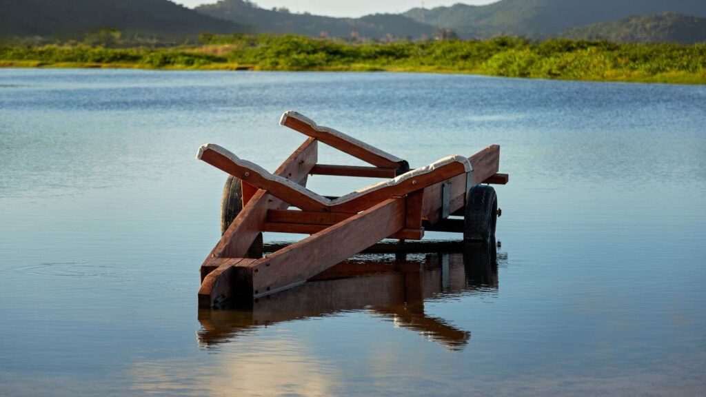 A wooden boat trailer partially submerged in calm water at a launch point