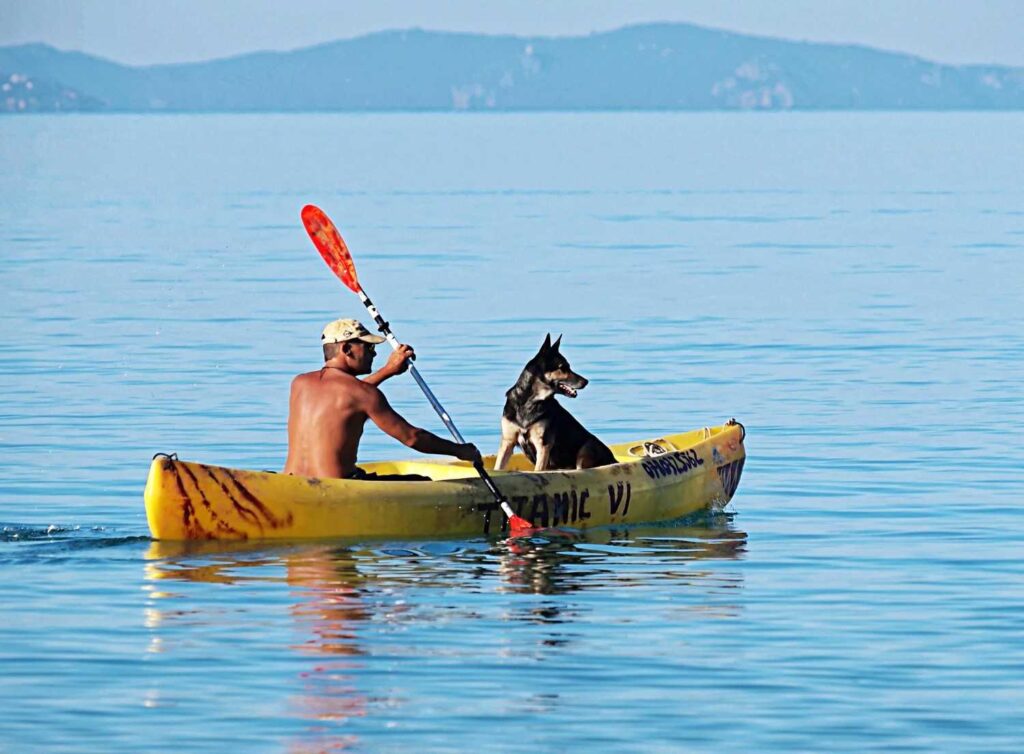 Man paddling a kayak with his dog on calm, still water with distant hills and no boat traffic