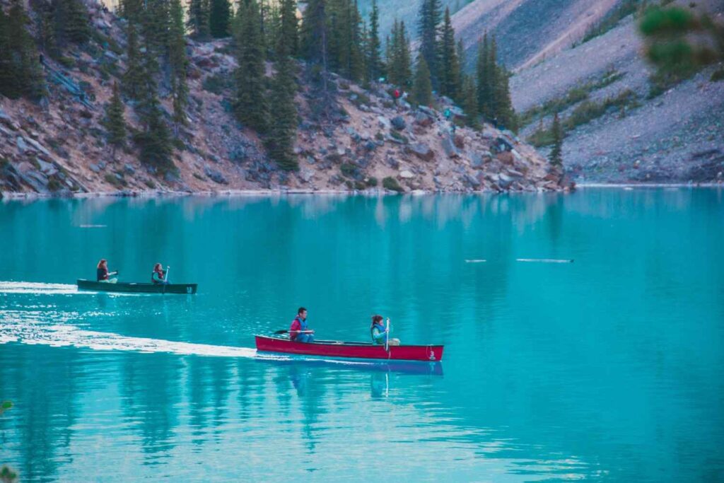 Two canoes each carrying two paddlers gliding across a turquoise mountain lake