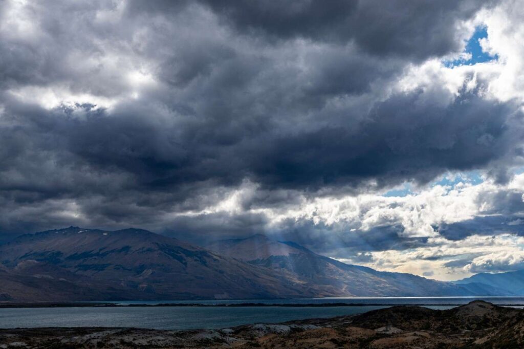 Dramatic dark storm clouds gathering over mountains and a calm lake, showing quickly changing weather