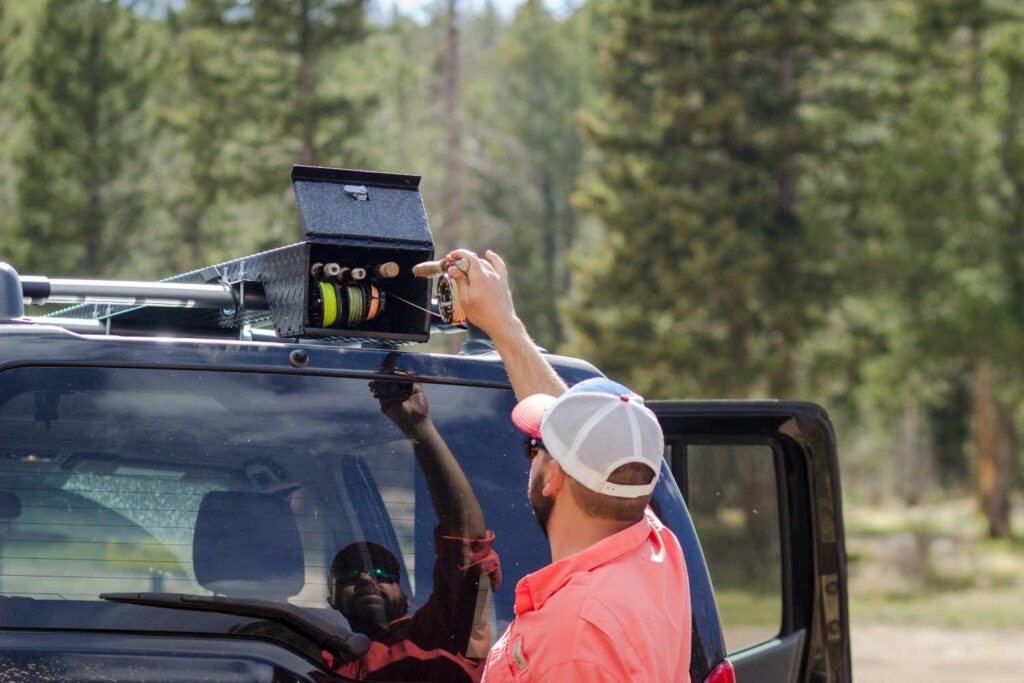 A person reaching up to adjust and check equipment mounted on a vehicle's roof rack crossbars