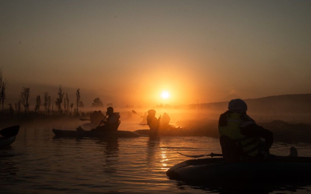 Group of kayakers paddling together through misty water at sunrise on a cold autumn morning