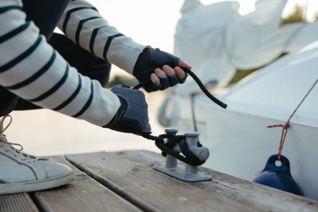 Close-up of a fingerless sailing glove gripping and tying a rope on a boat deck, showing textured grip design