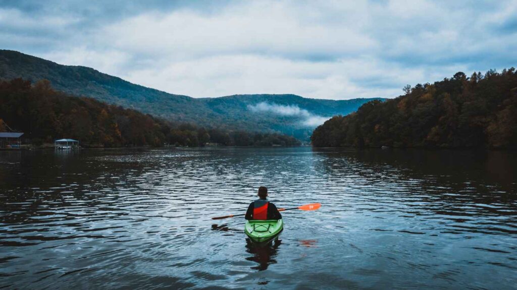 Kayaker paddling across a misty, cool mountain lake on an overcast autumn day