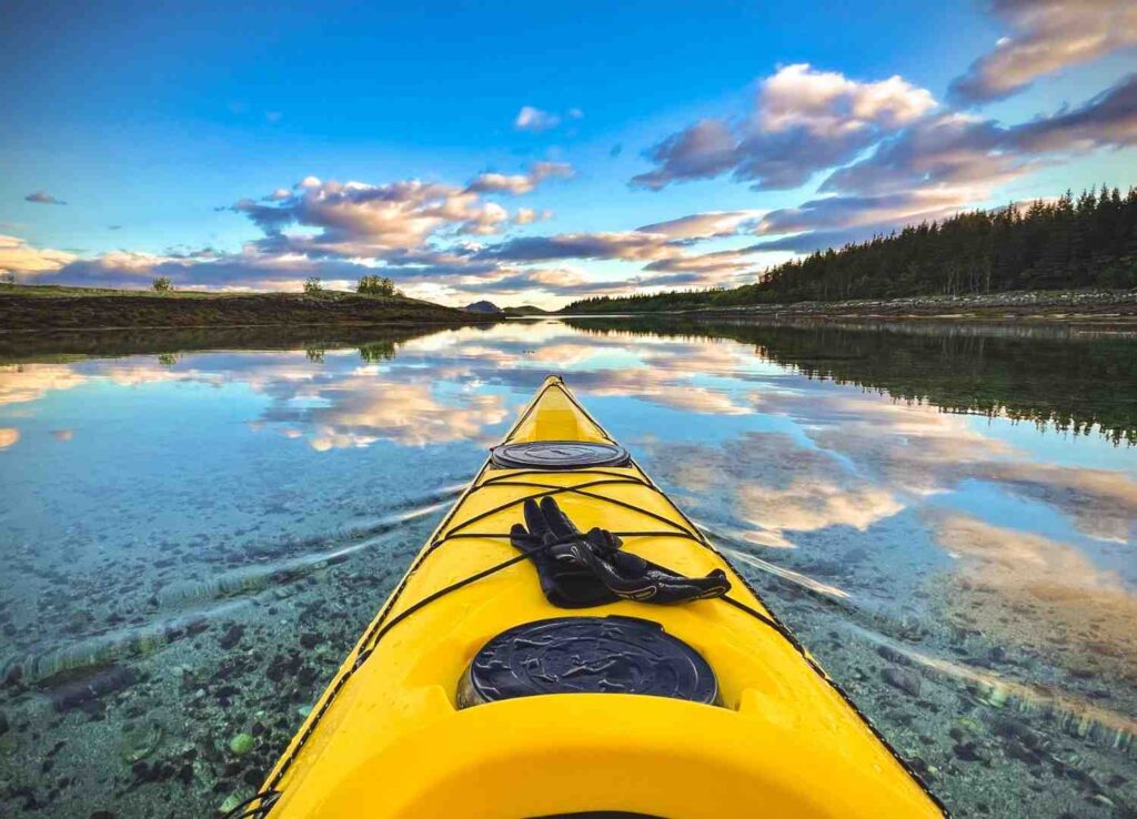 A pair of black neoprene kayak gloves resting on the bow of a yellow kayak at sunset