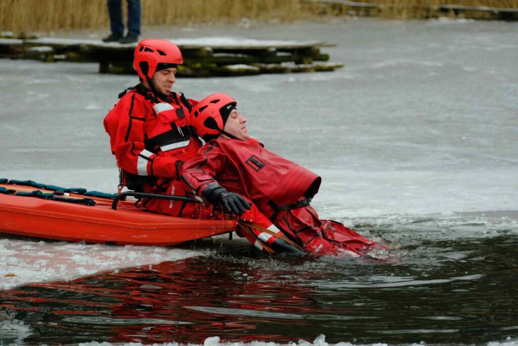 Two people in red immersion suits and helmets practice a cold-water rescue on an icy lake