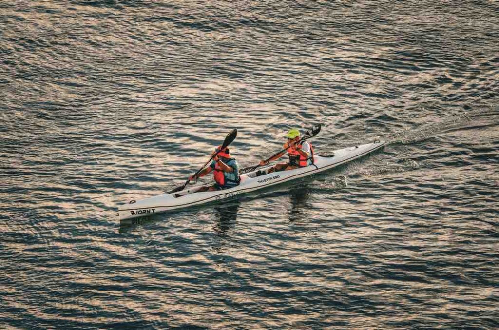 Two paddlers power a tandem kayak across open water with visible splash and speed