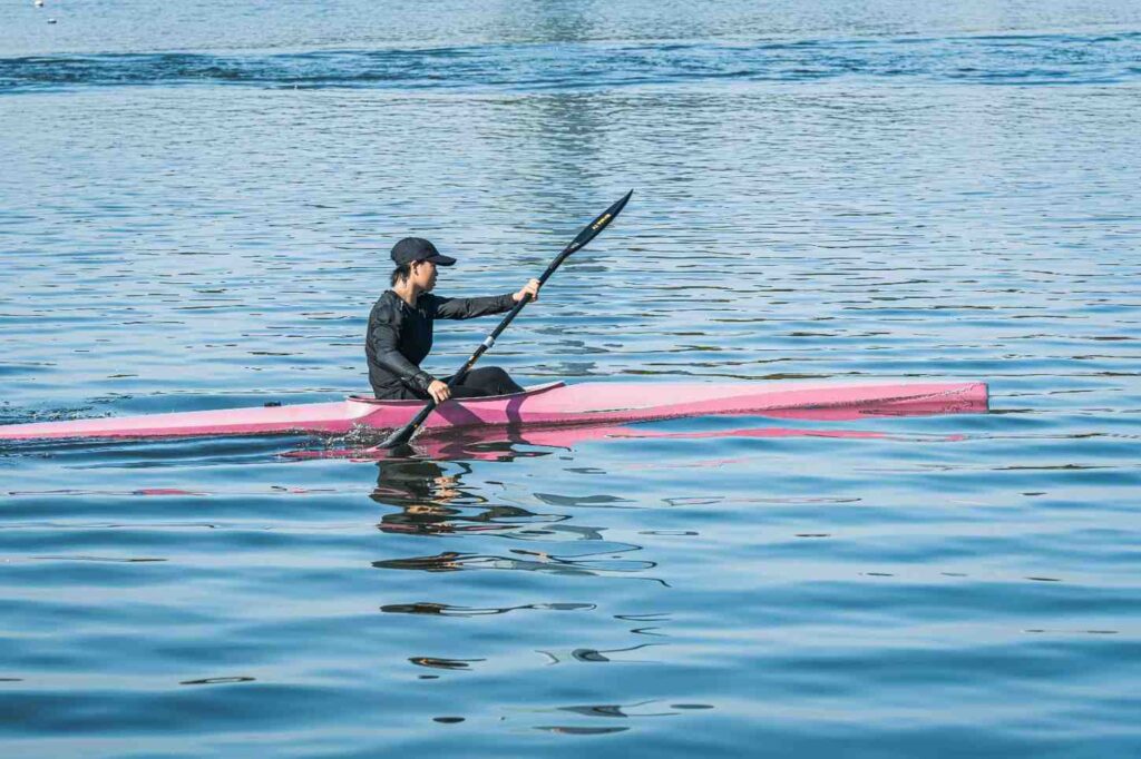A paddler in a pink performance kayak paddles efficiently across calm blue water