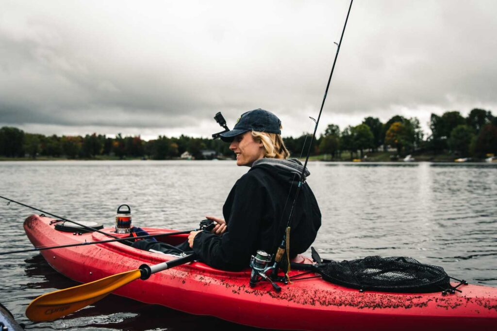 Angler on a red fishing kayak with multiple rod holders, reels, and a landing net attached