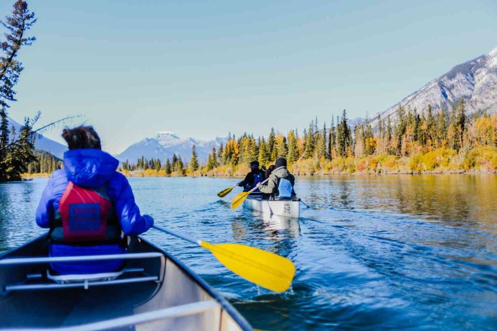 Multiple canoes with paddlers moving together down a river surrounded by autumn trees and mountains