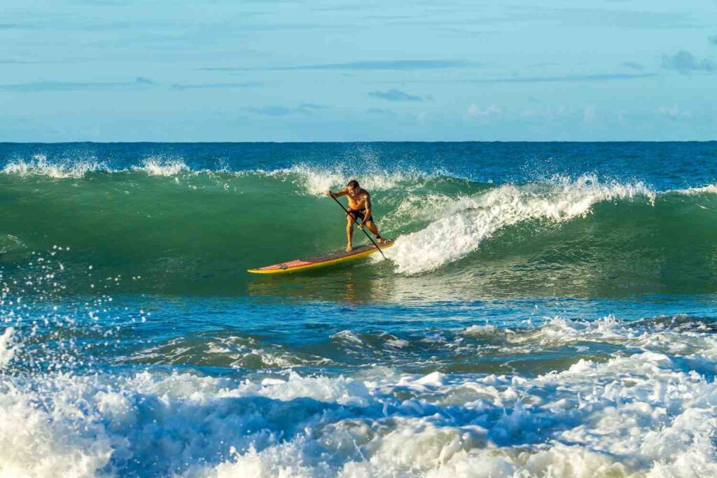Man aggressively paddleboarding on a large breaking wave, showing high-intensity SUP effort