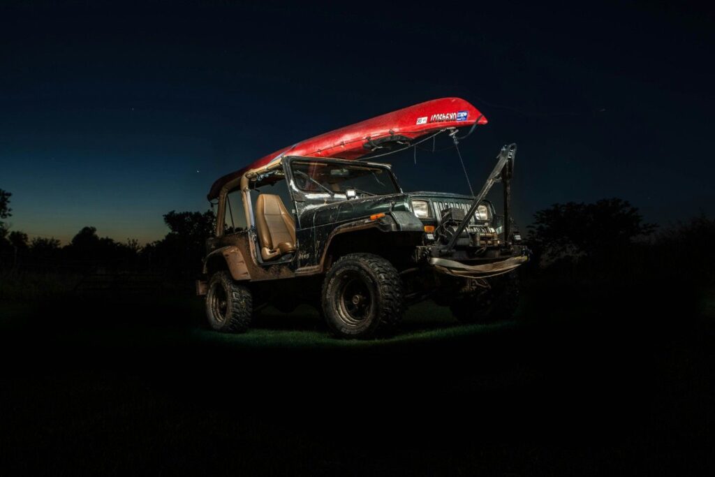 Jeep Wrangler with a kayak tied directly to its roll bar frame using ropes, without a proper crossbar rack system