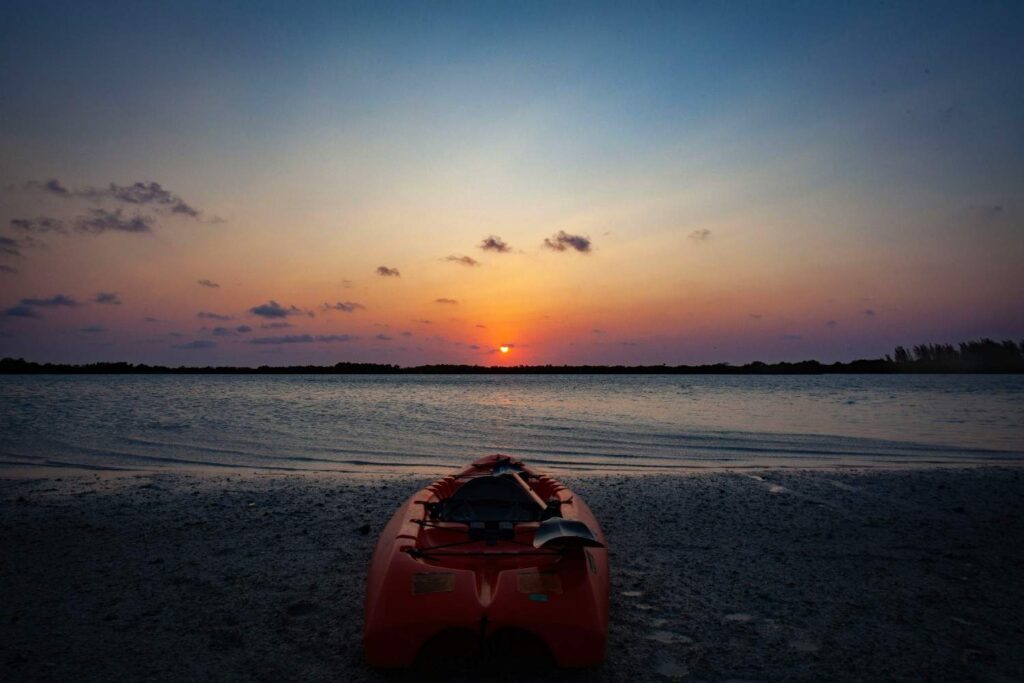 A kayak with paddle resting on the beach at sunset after a successful trip