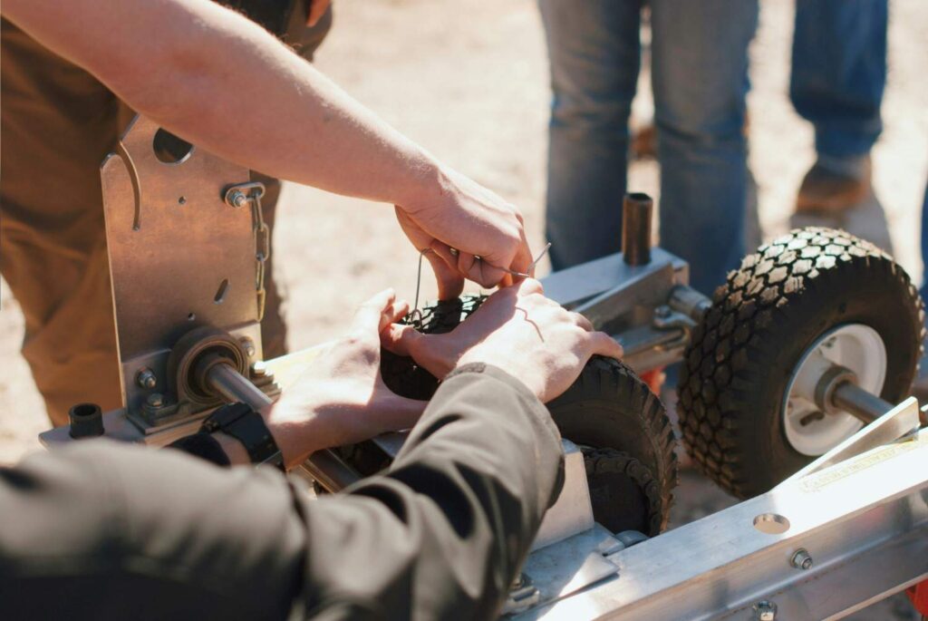 Two hands working on a wheel and chain axle mechanism during cart maintenance and repair