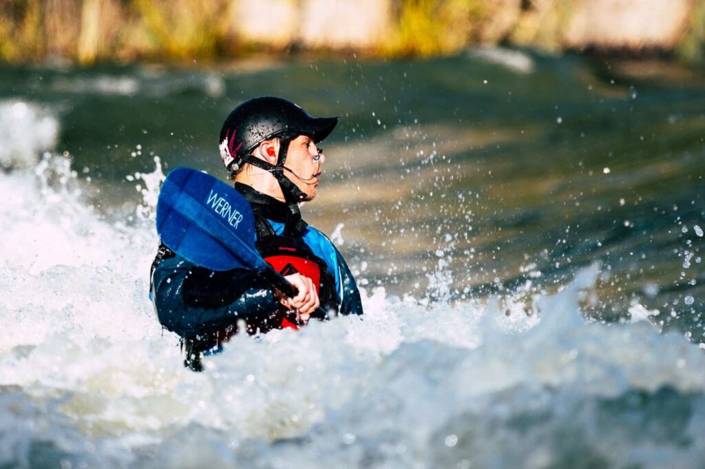 Close-up of a kayaker wearing a black helmet while surrounded by splashing whitewater