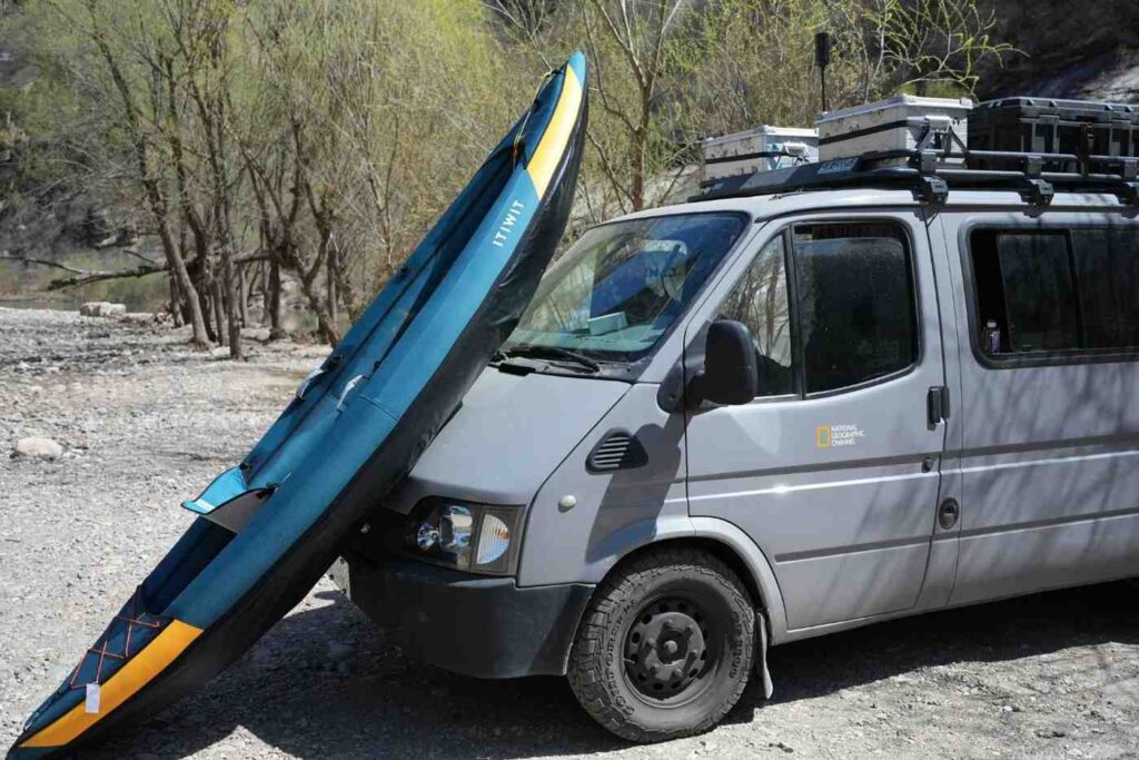 An inflatable kayak leaning against the front of a van, ready to be loaded onto the roof rack