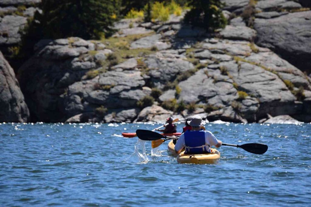 Kayakers paddling near a rocky lake shoreline with water dripping off the paddle blade mid-stroke