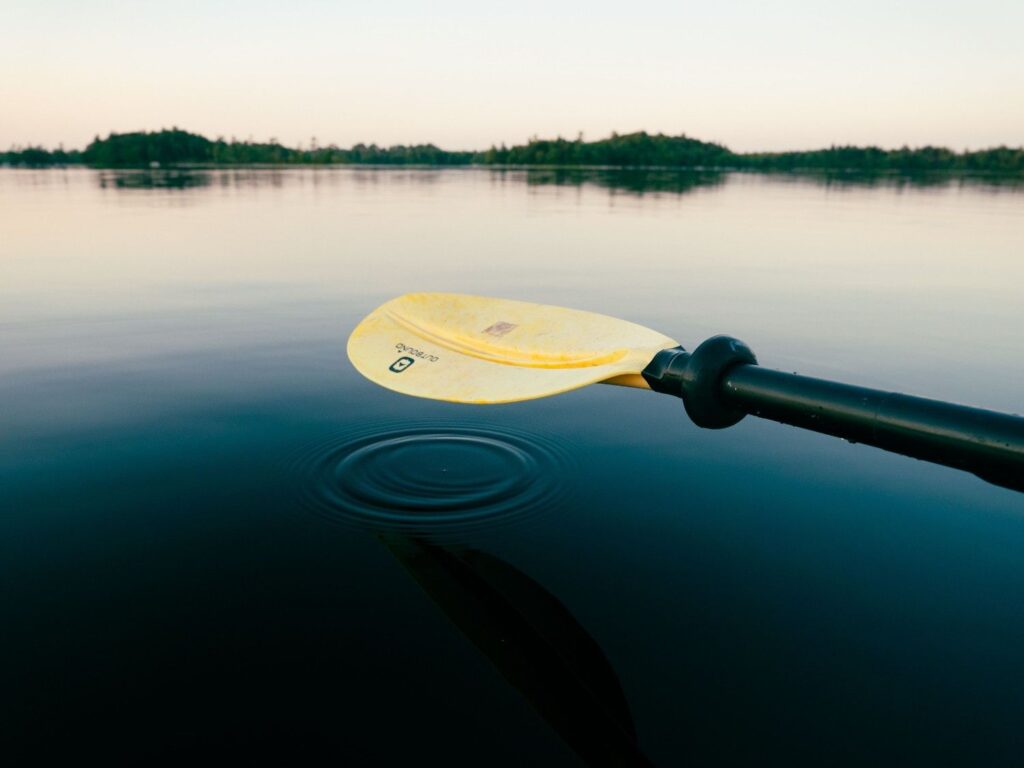 Close-up of a lightweight kayak paddle blade held just above calm water, creating a small ripple