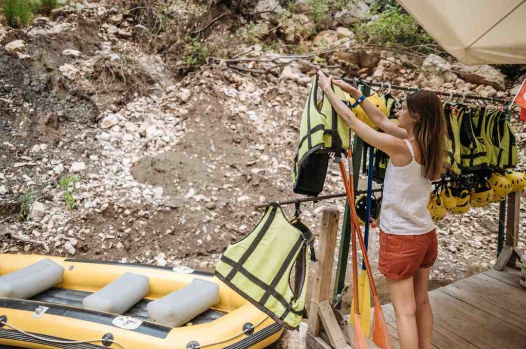 Woman selecting a life jacket from a rental gear rack with paddles and helmets nearby